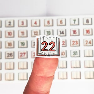 May include: A white sticker with a book illustration and the number 22 in red. The sticker is part of a set of numbered stickers with book illustrations.