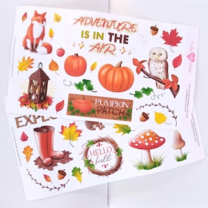 May include: Two sticker sheets featuring autumn-themed illustrations including a fox, pumpkins, an owl, a lantern, red rain boots, a mushroom, and a wreath. The text reads ADVENTURE IS IN THE AIR, PUMPKIN PATCH, HELLO FALL, and EXPLORE.