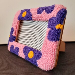 Set of handmade punch needle 4x6 picture frames featuring colorful daisy designs. Crafted with soft yarn, these frames add a cozy vibe to any space. Perfect for displaying cherished photos or as a unique decorative piece. Not wall-mounted.