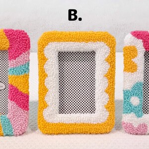 May include: Three colorful, handmade photo frames with different designs. The first frame has a striped design in pink, yellow, and blue. The second frame has a white scalloped border with a yellow background. The third frame has a white background with pink, yellow, and blue flowers.