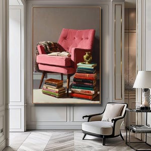 May include: A framed painting shows a pink armchair with a stack of books and a small gold vase. A patterned blanket and an open book rest on the chair. More books are stacked on the floor, creating a cosy reading nook.
