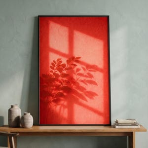 May include: A rectangular wall art piece in a thin black frame featuring a vibrant red textured background. The artwork displays a dark, crisp shadow of a leafy plant cast across the surface, overlaid with the geometric shadow of a window pane.