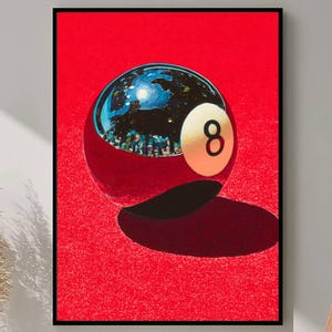 May include: A framed art print showing a reflective eight ball against a bright red backdrop. The eight ball's surface reflects a cityscape. The number eight is on a white circle. The print is in a black frame.