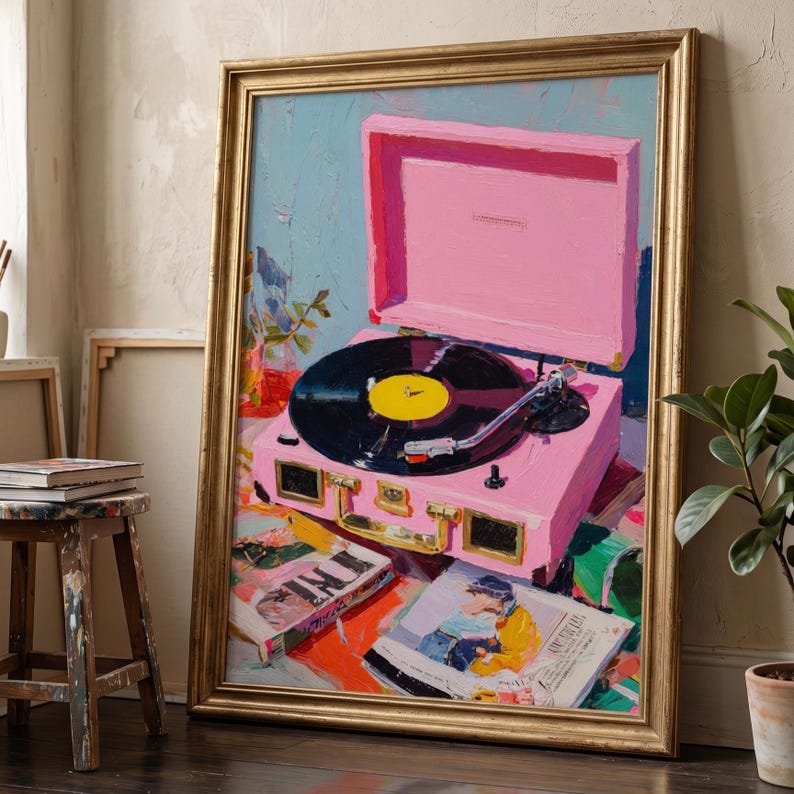 May include: A framed oil painting depicting a bright pink portable record player with a black vinyl record and yellow centre label. The scene includes scattered magazines and books beneath the turntable, all rendered in thick, textured brushstrokes.