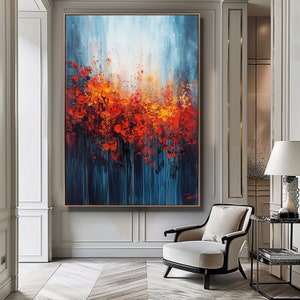 Puede incluir: Pintura abstracta con fondo azul y pinceladas rojas, naranjas y amarillas. La pintura está enmarcada y colgada en una pared de una habitación con una silla blanca y una mesa.