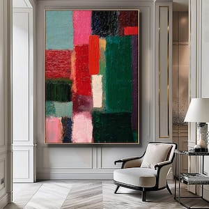 May include: Abstract oil painting on canvas featuring a vibrant composition of rectangular shapes. The artwork showcases a palette of colors including red, green, pink, and blue, with a gold frame. The painting is displayed in a well-lit room with a chair and side table.