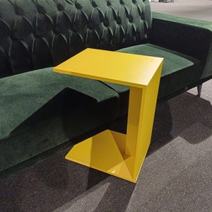 Könnte beinhalten: Ein leuchtend gelber Beistelltisch mit einem einzigartigen, modernen Design. Der Tisch hat eine rechteckige Tischplatte und ein geschwungenes, offenes Gestell.