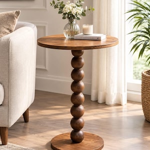 May include: A round wooden side table featuring a smooth circular tabletop and a central pedestal base composed of seven stacked wooden spheres, resting on a flat circular base. The wood has a medium brown finish with visible grain patterns.