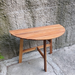 May include: A wooden half-circle table with a slatted top and a simple, sturdy base. The table is made of light brown wood and has a natural finish.
