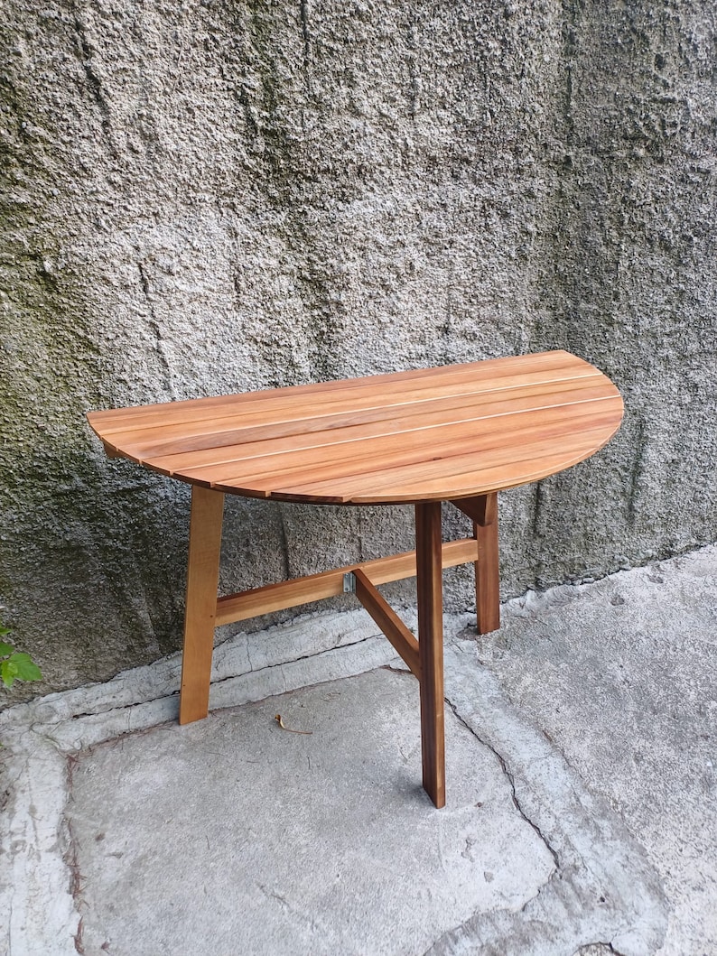May include: A wooden half-circle table with a slatted top and a simple, sturdy base. The table is made of light brown wood and has a natural finish.