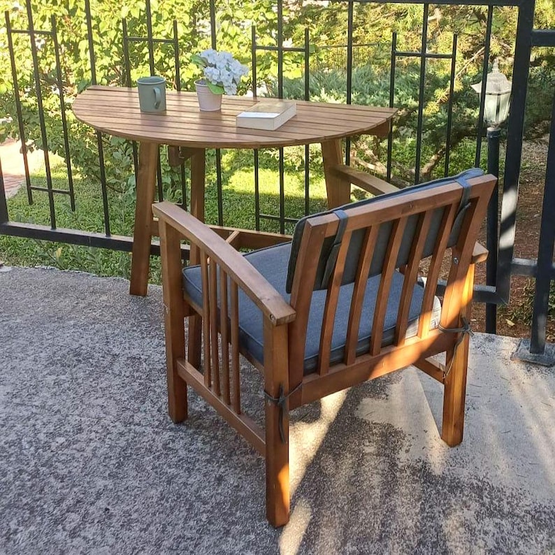 May include: A wooden patio set with a round table and a chair. The table has a wood top and a brown metal frame. The chair has a dark gray cushion and a brown wooden frame.