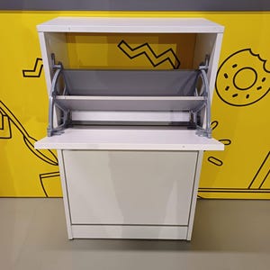 May include: White shoe storage cabinet with two shelves that fold down. The cabinet has a simple design and is made of wood.