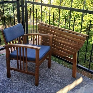 May include: A wooden folding table with a semi-circular top and a matching wooden chair with a blue cushion. The table and chair are on a gray concrete patio.