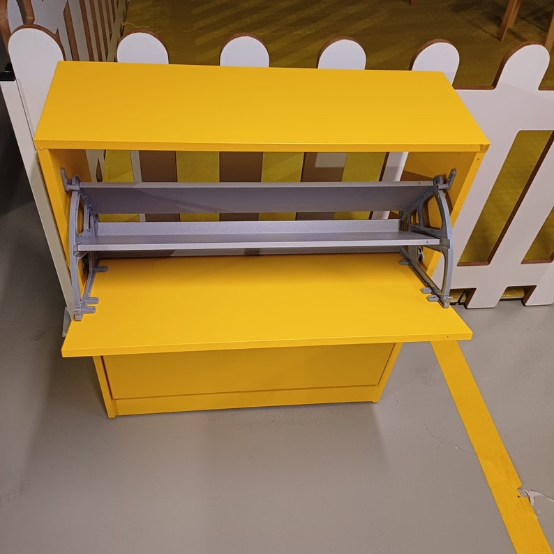 May include: A yellow wooden shoe rack with two shelves and a hinged door. The shelves are made of a light gray material and the door is closed.