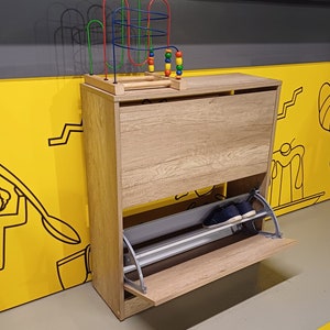 May include: A wooden shoe rack with a pull-out shelf. The shoe rack is light brown with a gray metal shelf. A colorful toy with beads is on top of the shoe rack.