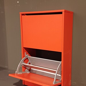 May include: A red shoe storage cabinet with a flip-down door and a pull-out shelf. The shelf is made of metal and has a silver finish.