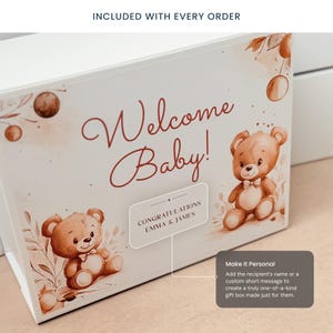 Może przedstawiać: Białe pudełko prezentowe z napisem "Welcome Baby!" w czerwonym skrypcie. Pudełko zawiera akwarelowe ilustracje misi&oacute;w i kwiatowych akcent&oacute;w. Etykieta głosi "Gratulacje Emma & James."