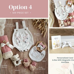 May include: A six-piece baby gift set in a white box with a magnetic closure and a bow. The set includes a white knitted romper with floral embroidery, a pink swaddle blanket, a white bib with floral embroidery, a rattle, a pair of socks with a cartoon bear design, and a headband with a bow.