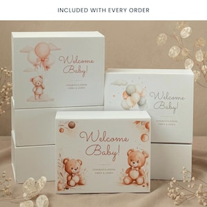 Może przedstawiać: Białe pudełka prezentowe z akwarelowymi ilustracjami i napisem "Welcome Baby!" w ozdobnej czcionce. Pudełka przedstawiają misie, balony i imiona "Emma & James". Pudełka są ułożone w stos.