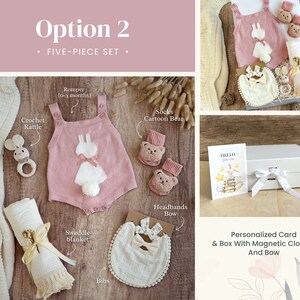 May include: A five-piece baby gift set in a white box with a pink romper, white crochet rattle, white swaddle blanket, white bib, and pink socks with a cartoon bear design. The box has a white ribbon and a personalized card that says "HELLO Little One".