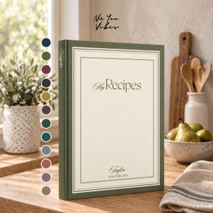 Puede incluir: Un libro de recetas de tapa dura con lomo y borde verde salvia, con una cubierta color crema con el texto My Recipes, Taylor y NEW YORK 2026. A la izquierda del libro se muestra una columna vertical de doce muestras de color circulares.