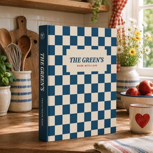 May include: A hardback recipe book featuring a blue and cream chequered pattern. The front cover includes a central cream label with the text THE GREEN'S and MADE WITH LOVE. The spine displays the text THE GREEN'S and FAMILY RECIPE BOOK.