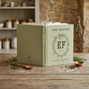 Personalized recipe book for couples in mint  hardcover, monogram EF inside a hand drawn botanical wreath, Cook Together above and the names Elizabeth and Fitzwilliam with their wedding date below, spine and back cover shown.