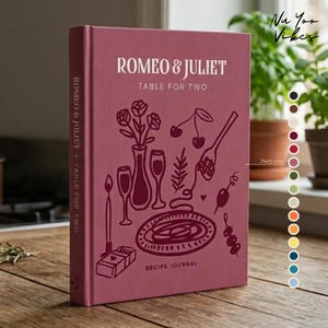 May include: A dusty rose hardcover recipe journal titled Romeo & Juliet Table for Two. The cover features dark maroon line art illustrations of a vase with roses, wine glasses, a candle, a plate of pasta, cherries, and a skewer of olives.