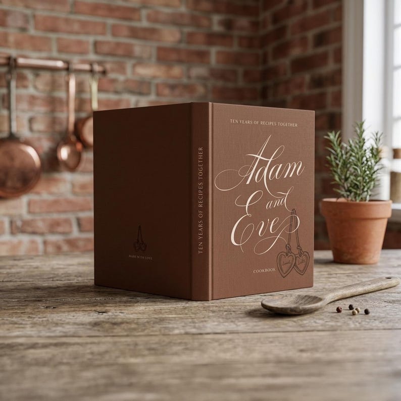 Personalized recipe book for couples in espresso brown  hardcover, the names Adam and Eve in flowing cream calligraphy with two heart lockets, Ten Years of Recipes Together on cover and spine.