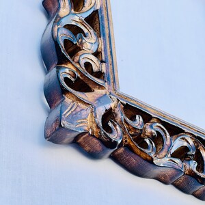 May include: A close-up of a wooden mirror frame with intricate carvings. The frame is a dark brown color with gold accents. The mirror is rectangular and has a beveled edge.