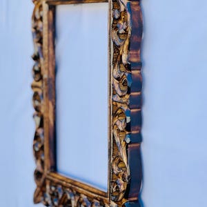May include: A brown wooden picture frame with intricate carvings. The frame has a gold finish and a rectangular shape.