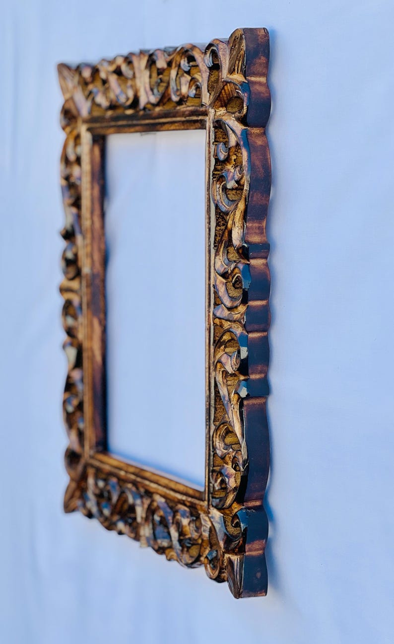 May include: A brown wooden picture frame with intricate carvings. The frame has a gold finish and a rectangular shape.