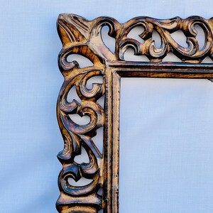 May include: A brown wooden picture frame with intricate carvings. The frame has a rectangular shape and a distressed finish.