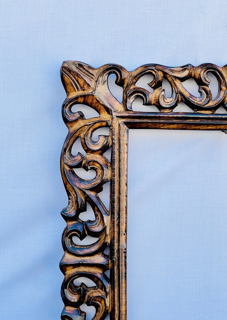 May include: A brown wooden picture frame with intricate carvings. The frame has a rectangular shape and a distressed finish.