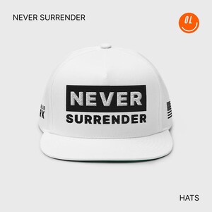 May include: White flat-brimmed hat with the words "NEVER SURRENDER" in a black rectangle. The hat has a small American flag design on the side and the word "HATS" at the bottom.