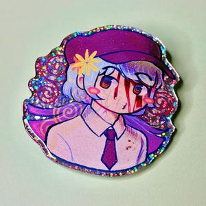 May include: A colorful anime-style pin featuring a character with light blue hair, a purple hat, and a white shirt with a purple tie. The character has red streaks on their face and a yellow flower on their hat. The pin has a glittery border.