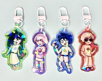 May include: Four character keychains with white metal clasps. Each keychain features a different cartoon character in various colors: green, purple, blue, and red. The characters are wearing different outfits and have unique poses.