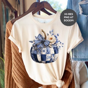 May include: A cream-coloured t-shirt with a blue and white patchwork pumpkin design, a gingham bow, and floral accents. The t-shirt is displayed on a wooden hanger. The image includes the text "HI-RES PNG AT 300DPI".