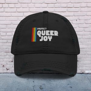 May include: Black distressed baseball cap with a rainbow and the text "PROTECT QUEER JOY" embroidered on the front.