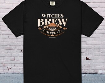 Puede incluir: Camiseta negra con un gráfico de una calavera con un sombrero y el texto "Witches Brew Coffee Co. Est 1684"