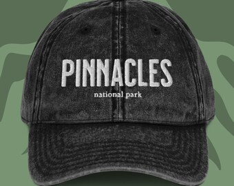 May include: Black distressed denim baseball cap with white embroidered text that reads "PINNACLES national park".