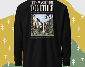 Op de afbeelding: Zwart longsleeve shirt met een grafische print van een waterval in een bos. De tekst "Let's Waste Time Together" is gedrukt op de achterkant van het shirt. De tekst "Peak Melodies Nature Therapy Tour Winter 2023" is gedrukt onder de afbeelding.
