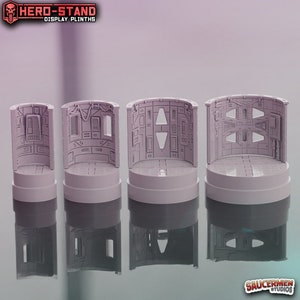 Puede incluir: Cuatro pedestales de exhibición de plástico gris con un diseño de ciencia ficción. Los pedestales están diseñados para sostener figuras en miniatura u otros objetos de colección. El texto "HERO-STAND DISPLAY PLINTHS" es visible en la parte superior de la imagen.