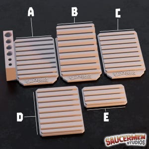 May include: A collection of beige, slatted, rectangular objects, possibly components for a larger structure. The objects vary in size, with one featuring a side piece with multiple holes. The "SAUCERMEN STUDIOS" logo is visible on the base of some pieces.