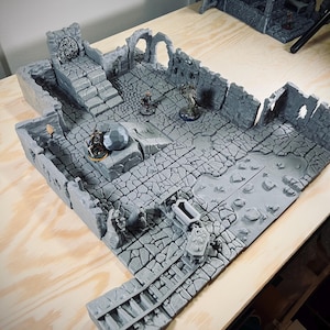 Peut inclure: Un ensemble de terrain de donjon gris imprimé en 3D avec des murs en pierre, des escaliers et un sol fissuré. Comprend des figurines miniatures, un gros rocher et un coffre au trésor. Conçu pour les jeux de rôle sur table.