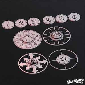 Könnte beinhalten: Ein Satz von neun 3D-gedruckten Spielsteinen, darunter sechs runde Token mit den Zahlen 1 bis 6, ein runder Stein mit einem kreisförmigen Design, ein runder Stein mit einem Sternendesign und ein runder Stein mit vier Pfeilen, die in verschiedene Richtungen zeigen.