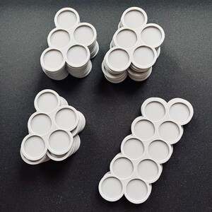 May include: Four stacks of light gray, circular objects with a honeycomb pattern in the center. Each object has seven connected circles. The objects are arranged on a dark surface.