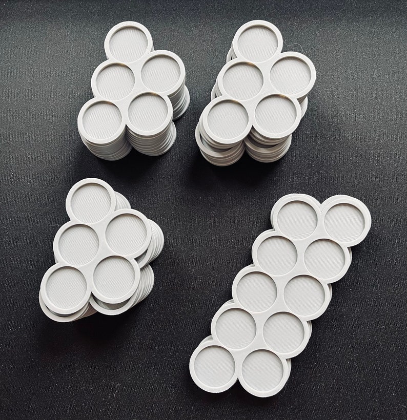 May include: Four stacks of light gray, circular objects with a honeycomb pattern in the center. Each object has seven connected circles. The objects are arranged on a dark surface.