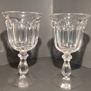 May include: Two clear glass wine goblets with a fluted design and a round base.