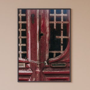 May include: A close-up of a red wooden door with a metal chain and lock. The door has a decorative metal grate and is weathered and worn.